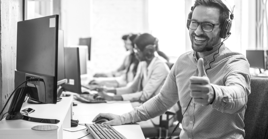  A smiling man wearing a headset is focused on his work at a computer, showcasing a positive work environment.