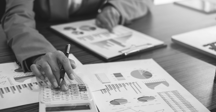 A black and white image of a business professional focused on calculations using a calculator at their desk.